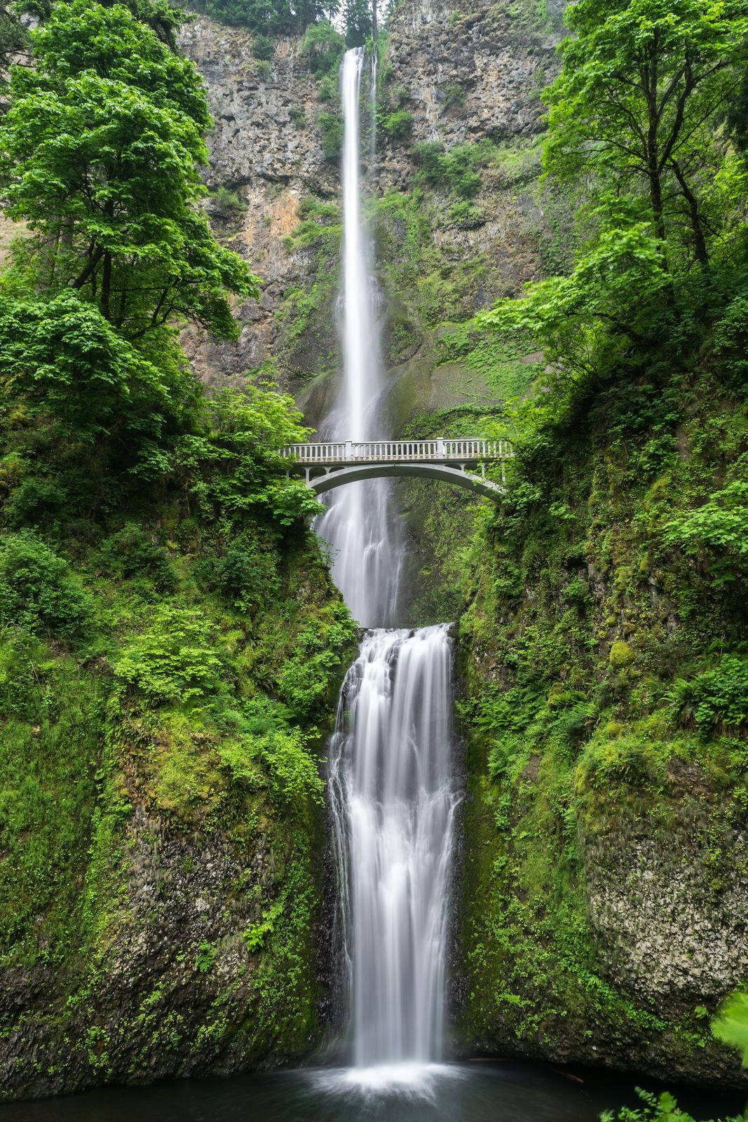 Tall waterfall under a stone bridge